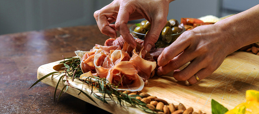 Woman's hands assembling cured meat presentation on charcuterie board.
